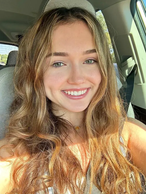 A young woman with long wavy hair smiling in a sunlit car.