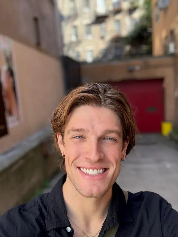 A young man smiling to camera in a city courtyard.