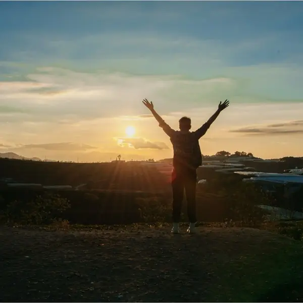 A person standing with arms raised towards a sunrise.