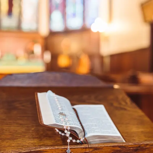 An open Bible resting on a wooden pew with a rosary beside it.
