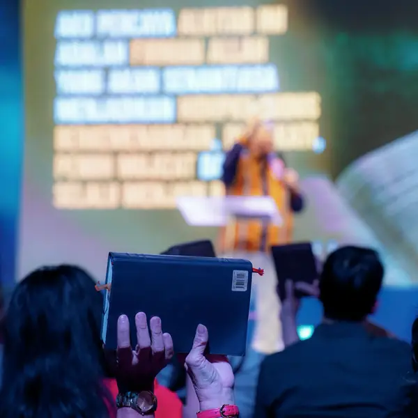 Someone speaking to a congregation in front of a projector screen.