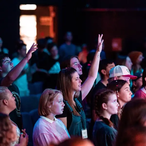 Young people at a worship gathering with their hands raised.